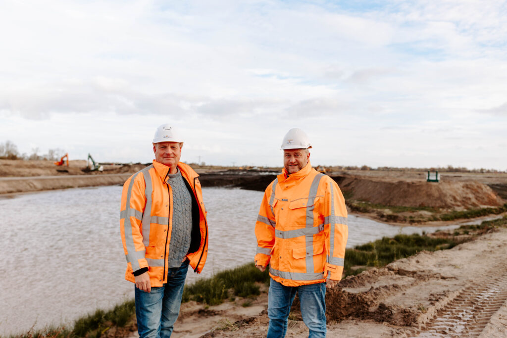 Vacature projectleider civiele techniek: Twee mannen bespreken plannen bij een civieltechnisch project aan het water.
